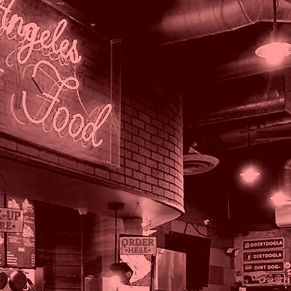 Interior view of a restaurant with a neon "Street Food" sign and exposed industrial ceiling.