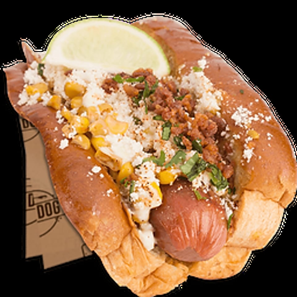 Gourmet hot dog with corn, cheese, crumbled chorizo, cilantro, and a lime wedge.