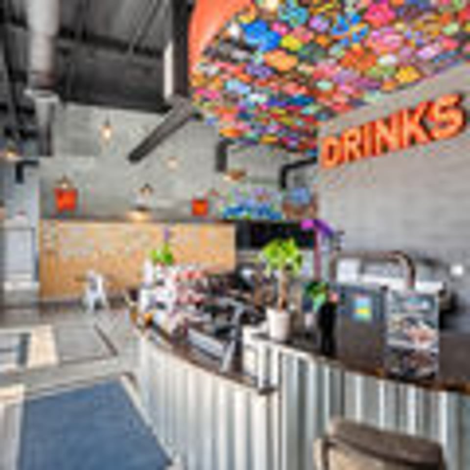 Modern restaurant interior with a colorful ceiling, a bar counter, and a "DRINKS" sign.